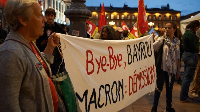 Gente en medio de protestas con pancartas pidiendo la dimisión del presidente francés Emmanuel Macron.